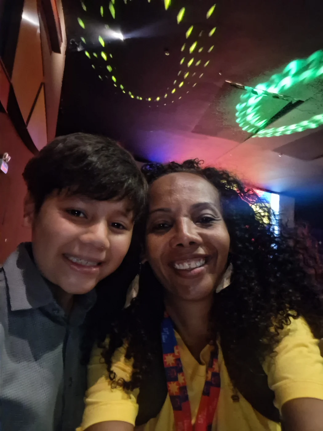 Simone Borges em uma selfie ao lado de uma criança, em um ambiente com iluminação colorida